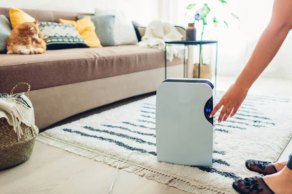 Mulher vira desumidificador em usar o painel de toque em casa. Dispositivo de secador de ar moderno para limpar o ar — Fotografia de Stock