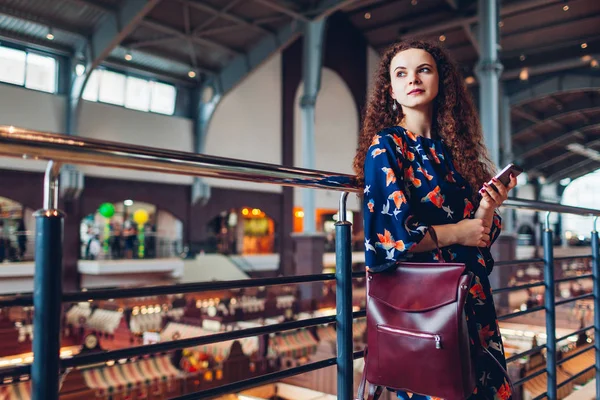 Молода жінка з рюкзаком використовує смартфон після покупки в торговому центрі — стокове фото
