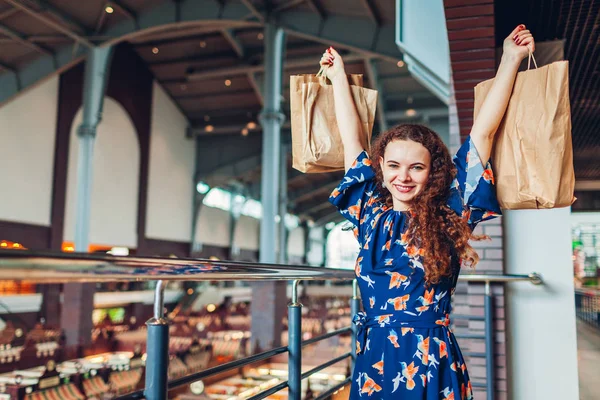 Joven mujer feliz levantando manos con bolsas de papel de compras en el centro comercial . — Foto de Stock