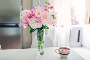 Masada çay olan pembe şakayıklar. Modern mutfak tasarımı. Çiçeklerle süslenmiş beyaz ve gümüş mutfak iç.