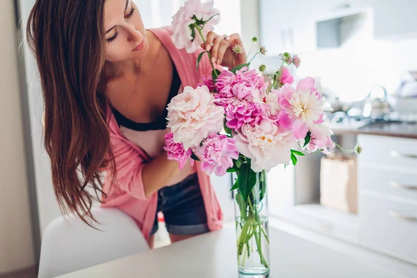 Kvinnan sätter pioner blommor i vas. Hemmafru tar hand om mysigt och dekor på kök. Komponera bukett. — Stockfoto