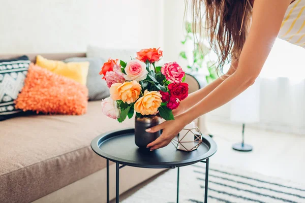 Mujer pone jarrón con flores rosas en la mesa. Ama de casa cuidando de la comodidad en el apartamento. Interior y decoración — Foto de Stock