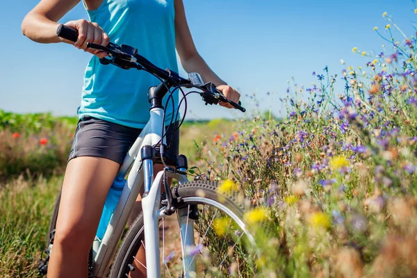 Young woman cyclist riding a mountain bicycle in summer field. Close up of handlebar