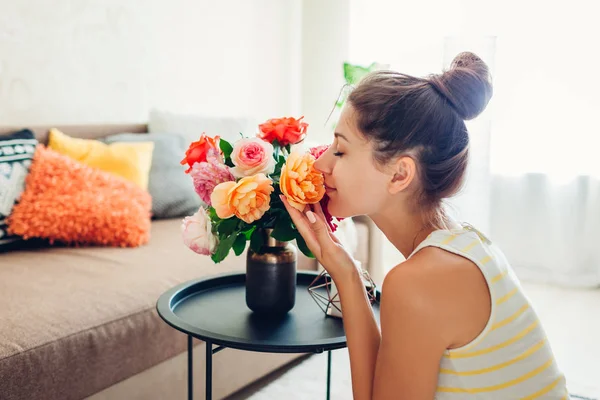 Kvinnan luktar färska rosor i vas på bordet. Hemmafru tar hand om mysigt i lägenheten. Interiör och inredning — Stockfoto