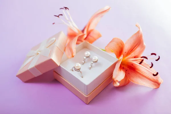 Conjunto de joyas de perlas en la caja de regalo con flores. Pendientes y anillo con lirio sobre fondo púrpura — Foto de Stock