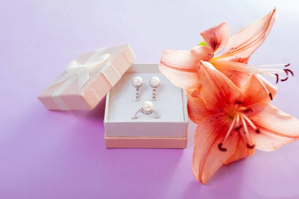 Conjunto de joyas de perlas en la caja de regalo con flores. Pendientes y anillo con lirio sobre fondo púrpura — Foto de Stock