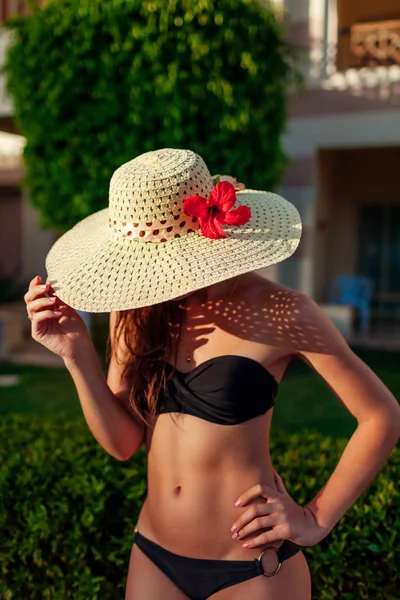 Sexy woman in black bikini hiding face with hat in hotel garden. Summer vacation on resort. — Stock Photo, Image