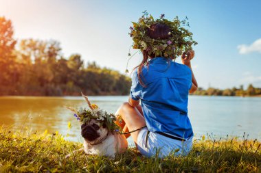 Pug köpek ve ana çiçek çelenk giyen nehir tarafından ürpertici. Mutlu köpek yavrusu ve kadın yaz doğa açık zevk