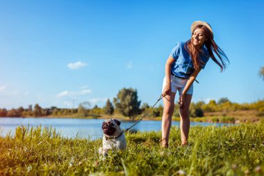 Nehir kıyısında oturan pug köpeği. Mutlu köpek yavrusu efendinin emrini bekliyor. Köpek ve kadın açık havada ürpertici