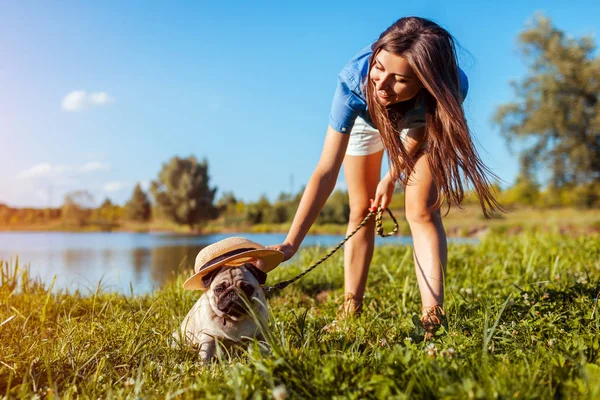 Un cagnolino seduto vicino al fiume mentre una donna ci mette il cappello. Felice cucciolo e il suo maestro camminare e rilassarsi all'aperto — Foto Stock