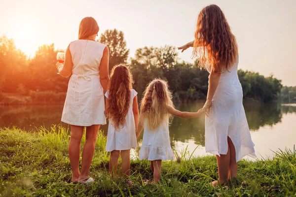 Family walking by summer river at sunset. Mother, grandmother and kids admiring landscape. Three denerations