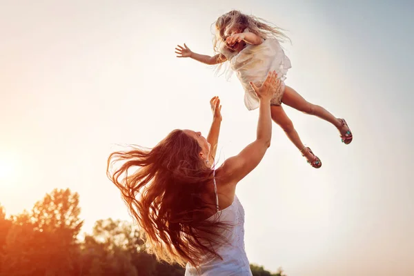Mulher brincando e se divertindo com a filha no parque de verão ao pôr do sol. Mãe jogando menina ao ar livre . — Fotografia de Stock
