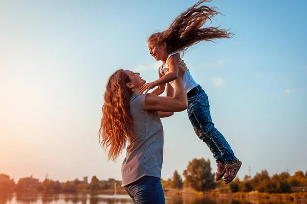 Mulher brincando e se divertindo com a filha no parque de verão ao pôr do sol. Mãe jogando menina ao ar livre e rindo . — Fotografia de Stock