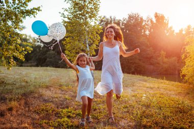 Küçük kız annesiyle koşuyor ve elinde baloon tutuyor. Yaz parkında eğlenen aile