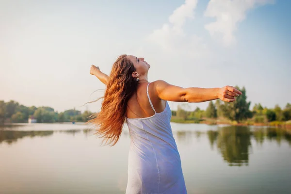 Mladá žena se cítí svobodná a šťastná, zvedá paže a točí se kolem letní řeky při západu slunce — Stock fotografie