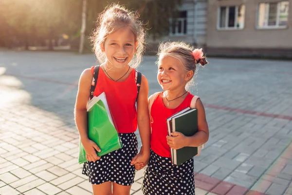 Jolies sœurs filles portant des sacs à dos et tenant des livres. Enfants élèves tenant la main à l'extérieur de l'école primaire. Éducation — Photo