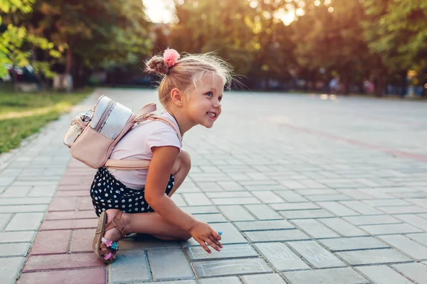 Jolie petite fille portant un sac à dos et dessinant avec de la craie à l'école primaire. Le gamin s'amuse après les cours — Photo