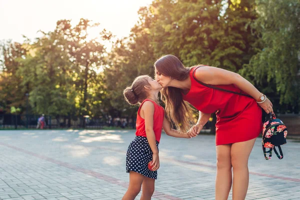 Счастливая мать встречается с дочерьми после занятий в начальной школе. Семейный поцелуй. Возвращение в школу — стоковое фото