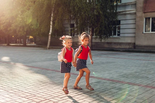 Sœurs heureuses filles portant des sacs à dos et courir. Enfants élèves s'amusant près de l'école. Éducation — Photo