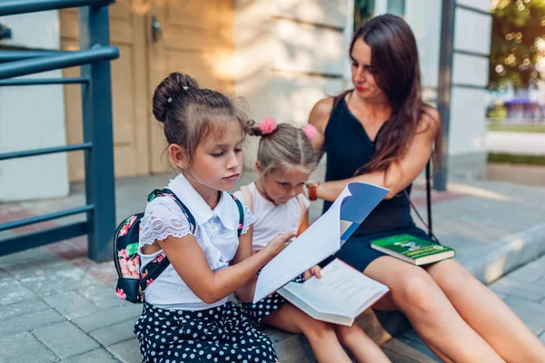 Bonne mère a rencontré ses enfants filles après les cours. Enfants lisant des livres en plein air école primaire . — Photo