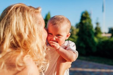 Genç anne yaz parkında kız bebek öpüşme ve sarılma. Dışarıda eğlenen aile