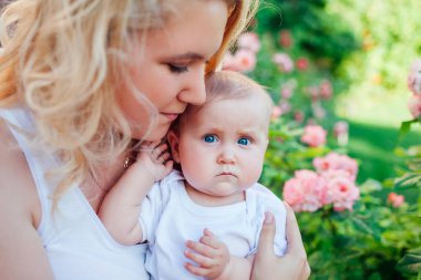 Gül bahçesinde bebek gir sarılma genç anne. Kameraya bakan bebek.