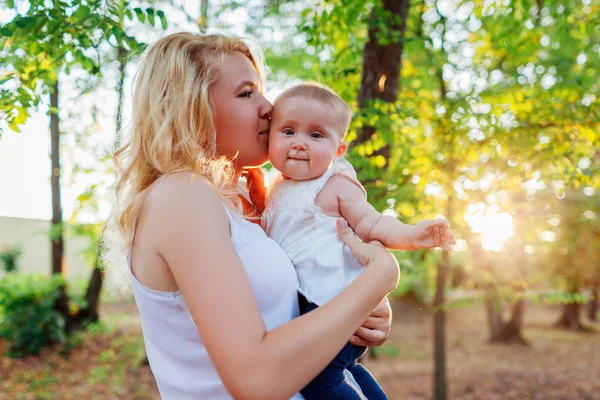 Genç anne bebeğiyle yaz parkında yürüyor. Mutlu kadın tutan ve çocuk açık öpüşme