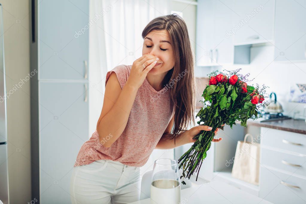 Woman takes dead roses out of vase feeling bad smell. Housewife taking care of coziness on kitchen.