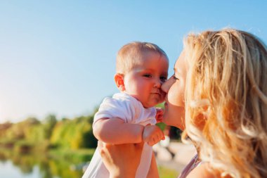Bebeği yüzüne yakın tutan genç bir anne. Parkta yürüyen aile