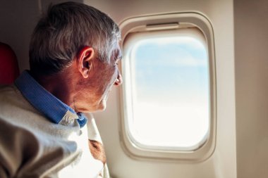 Kıdemli adam uçak penceresine bakıyor. Rahat business class koltuğunda oturan yolcu