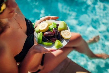 Kadın meyve yeme ve yüzme havuzunda rahatlatıcı bikini. Herşey dahil. Yaz tatili