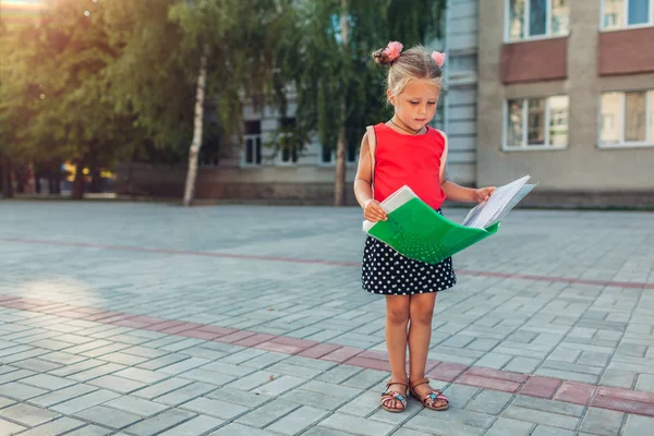 Joyeux élève portant un sac à dos et tenant un dossier. Enfant lisant en plein air école primaire. Éducation — Photo