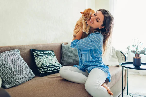 Играть с котом дома. Молодая женщина сидит на диване и обнимает питомца . — стоковое фото
