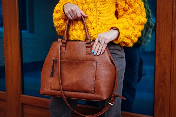 Handbag. Woman holding stylish bag and wearing yellow sweater. Autumn female clothes and accessories. Fashion
