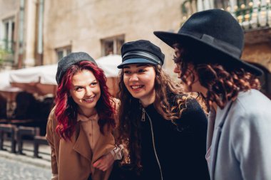 Arkadaşlar gülüyor ve eğleniyor. Şehir caddesinde konuşan üç şık genç kadının açık çekim.