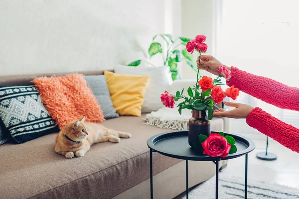 Mujer pone flores rosas en jarrón en la mesa. Ama de casa cuidando de la comodidad en el apartamento. Interior y decoración — Foto de Stock