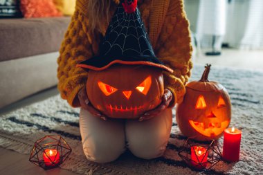 Cadılar Bayramı jack-o-fener kabakları. Kadın el yapımı oyma balkabağı tutar. Geleneksel sembollerle dekore edilmiş ev.