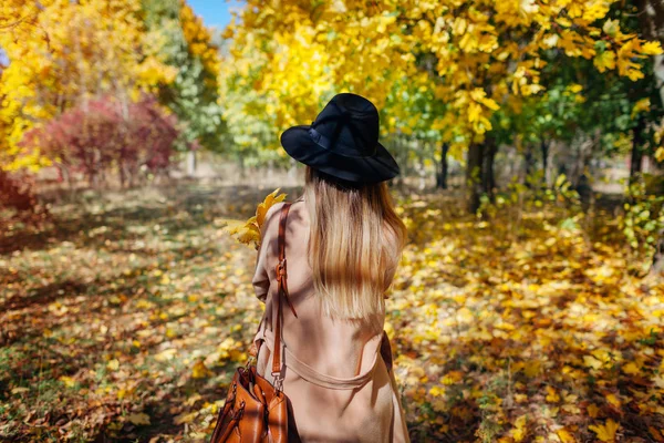 Podzimní vibrace. Mladá žena kráčí podzimním lesem mezi padajícími listy. Stylová dívka v klobouku — Stock fotografie