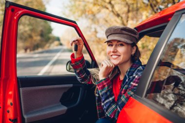 Kadının elinde yeni arabanın anahtarları var. Mutlu alıcı kırmızı otimobil satın aldı. Sürücü otomatik kameraya bakıyor.
