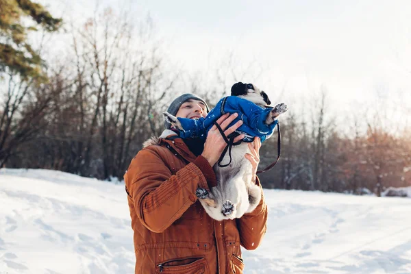 Mops beim Gassigehen mit seinem Herrchen. Mann spielt mit seinem Haustier und hat Spaß. Welpe im Wintermantel. — Stockfoto