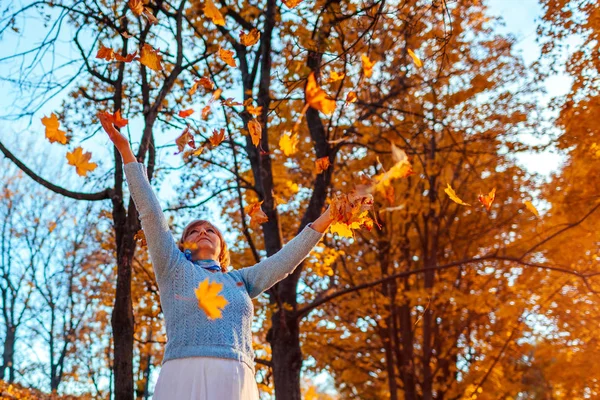 Fall season. Woman throwing leaves in autumn forest. Senior woman having fun outdoors — Stock Photo, Image