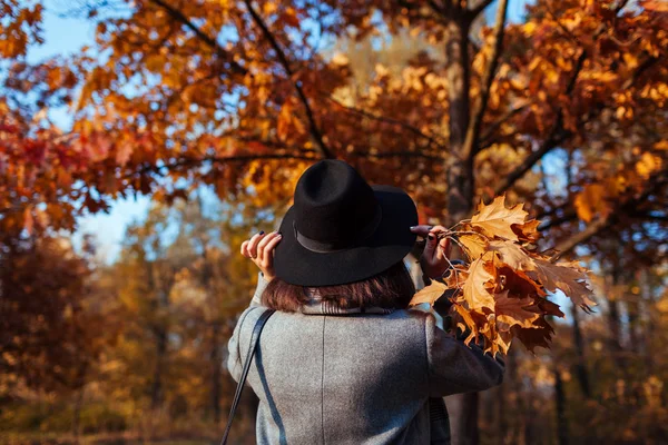 秋のシーズン秋の公園を歩く若い女性が自然を賞賛し、葉の花束を保持 — ストック写真