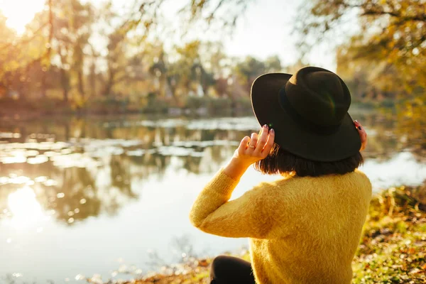 Мандрівник відпочиває осінньою річкою на заході сонця. Молода жінка сидить на березі і тримає капелюх — стокове фото