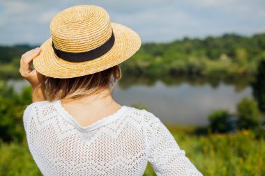 Yaz tarlasında nehirden tarlaya yürümekten zevk alan bir kadın. Kız, göl ormanı manzarasına hayran. Tatil seyahati