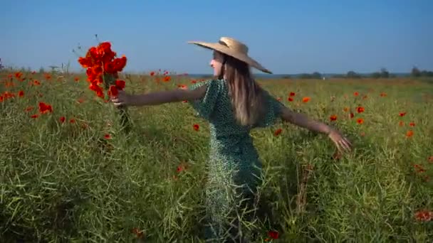 一个时髦的女人抱着一束鲜花在夏日的田野里散步 戴着草帽的快乐女孩欣赏风景 — 图库视频影像