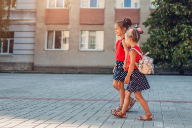 Okula giderken sırt çantası takan mutlu kız kardeşler el ele tutuşuyorlar. Eğitim. Okula geri dön.