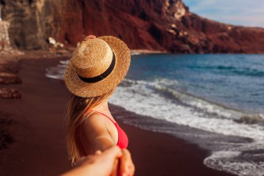 Beni takip edin. Santorini, Yunanistan 'da Red Beach' te bikinili, rahatlatıcı, seksi bir kadın. Kız, erkeğin elini tutuyor ve deniz manzarasının tadını çıkarıyor.