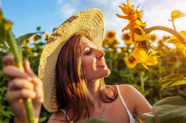 Genç, mutlu bir kadın çiçek tarlasında yürüyor, şapkasını takıyor, çiçekleri kokluyor ve manzarayı seyrediyor. Yaz tatili