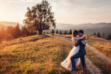 Güzel yeni evli çiftler gün batımında dağlarda birbirlerine sarılıyorlar. Gelin ve damat yazın Karpatlar 'da yürüyor. Düğün.