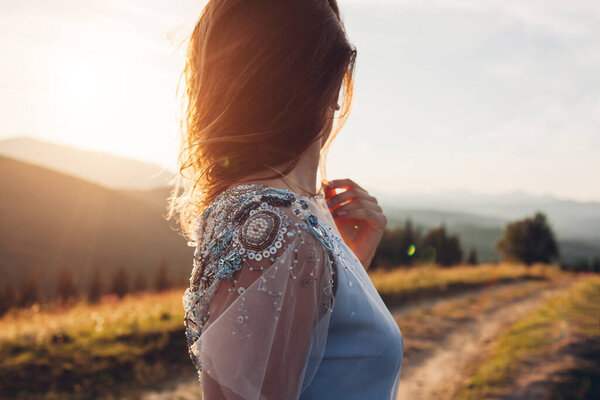 Beautiful bride wearing blue wedding dress in mountains at sunset. Young woman enjoys summer landscape. Close up of fashionable decor